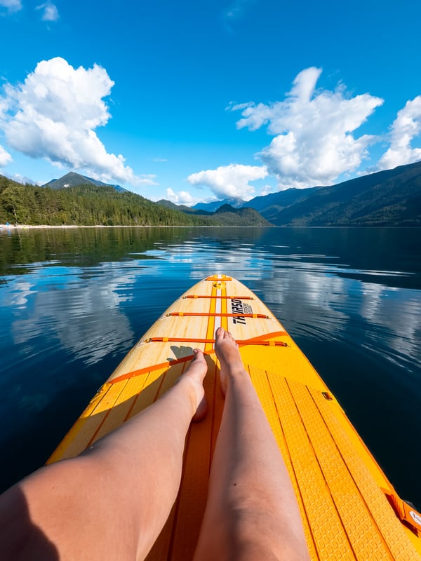 Woman sitting on a yellow paddleboard on a glassy lake