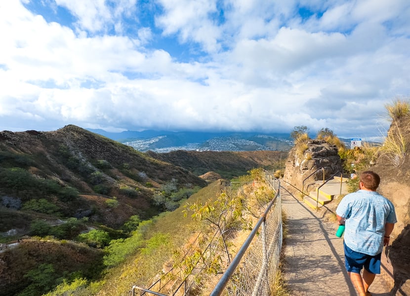 Man walks along the trail overlooking the crater walls of Diamond Head with Honolulu in the distance.