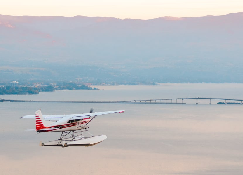 A closeup of a float plane with Okanagan lake and Bennett Bridge in the background.
