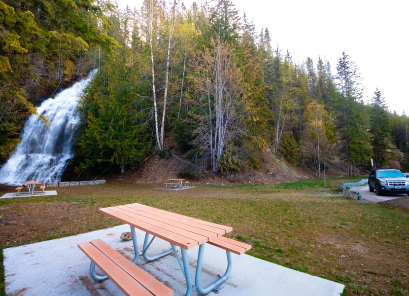 View of the picnic area, parking area, and waterfall at the Ione Rest Area near Nakusp, BC.