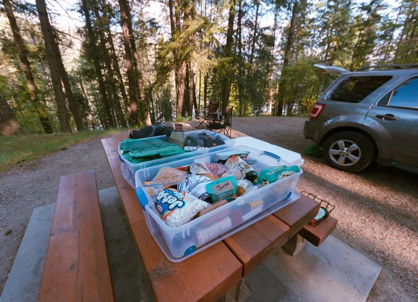 Food in a container on top of a picnic table at a campsite