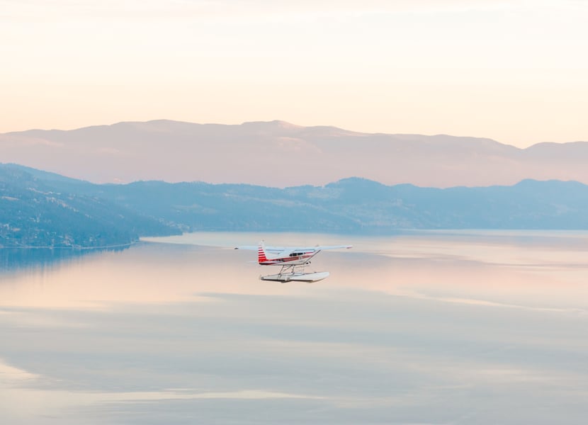 A floatplane flies over Okanagan Lake at sunset. 