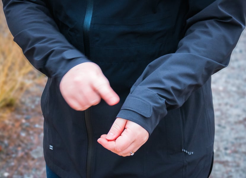 Woman adjusting velcro cuffs on a rain jacket, motion blur on one hand.