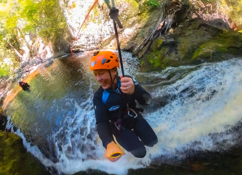 A woman ziplines down a waterfall in a canyon