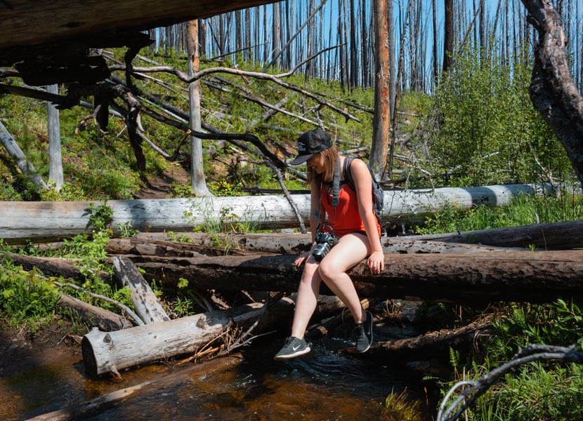 Woman scoots across a log crossing on the Christie Falls trail in Kelowna.