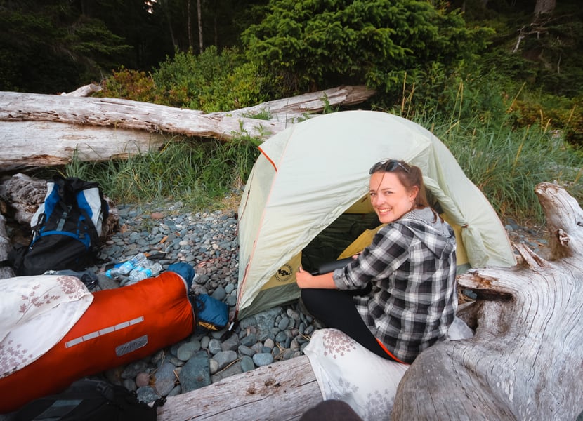 Woman setting up a tent on Mystic Beach, facing the trees with the forest in the background.