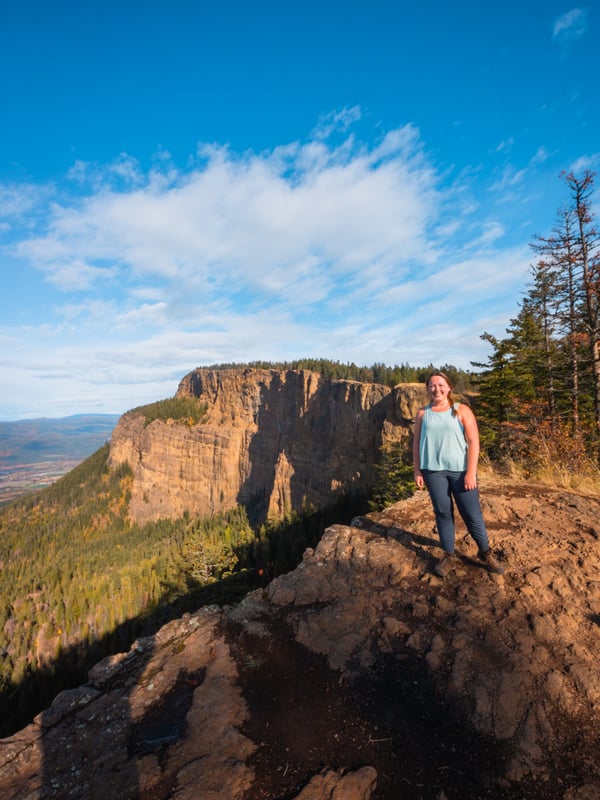 Woman standing at the top of the Enderby Cliffs hike with the foot-shaped cliffs in the background.