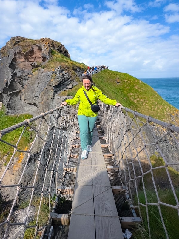 Woman walks across a rope bridge, high above the ocean floor in Northern Ireland