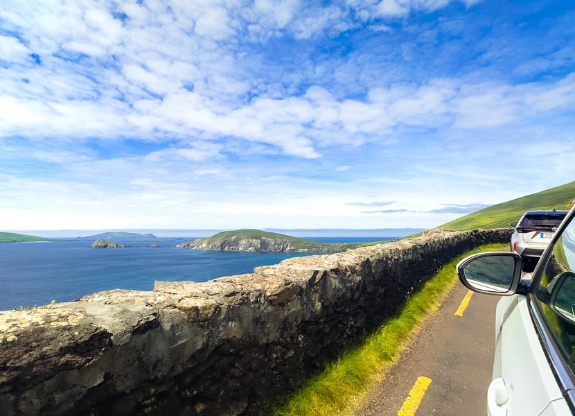 Car driving along a narrow road overlooking the ocean on the Slea Head Drive in Ireland.