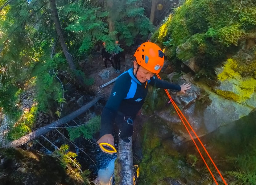 A woman walks over a log in a canyon