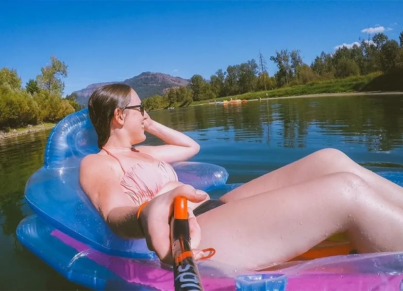 Selfie of a woman on a floatie on the Enderby River with the Enderby Cliffs in the background.