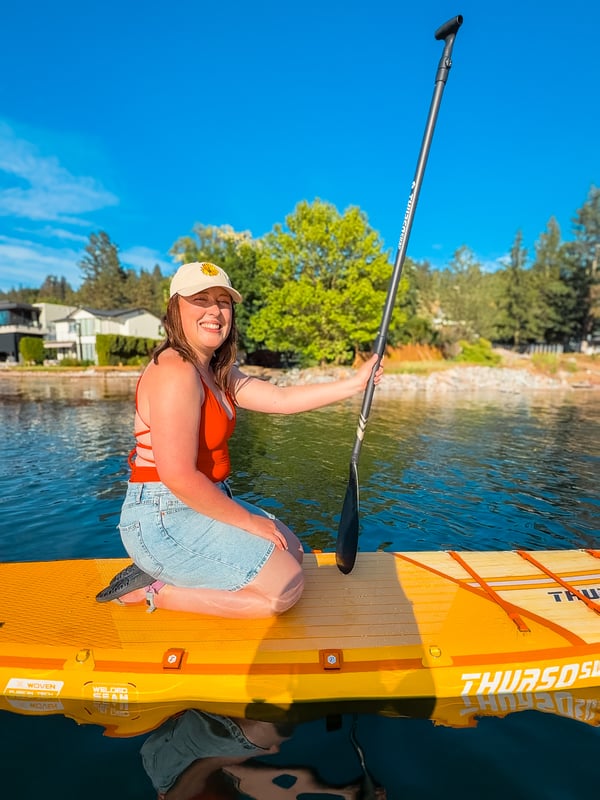Woman wearing a red Londre bathing suit kneeling on a yellow paddleboard on a lake