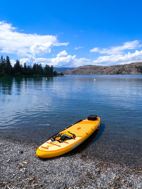 A yellow Thurso Surf paddleboard sitting on the edge of a lake
