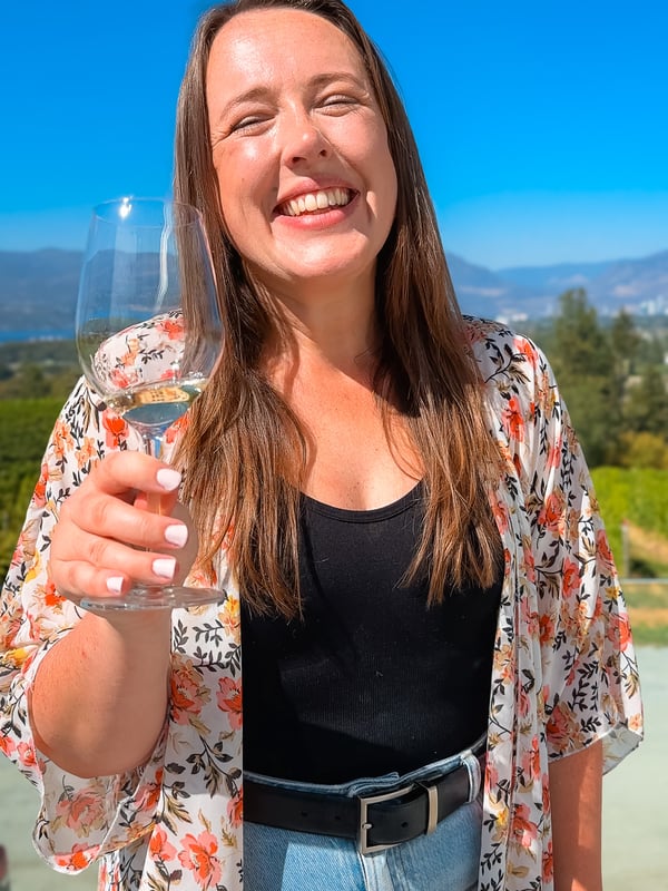A young woman holding a wine glass and smiling on a sunny day in Kelowna.