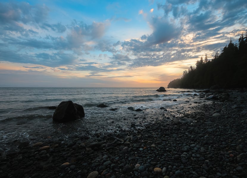 Sunset over Mystic Beach, with warm hues in the sky and the ocean gently lapping at the shore.