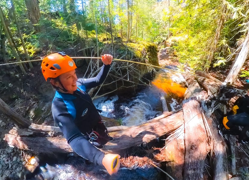 A woman walks over a fallen log while connected to a rope