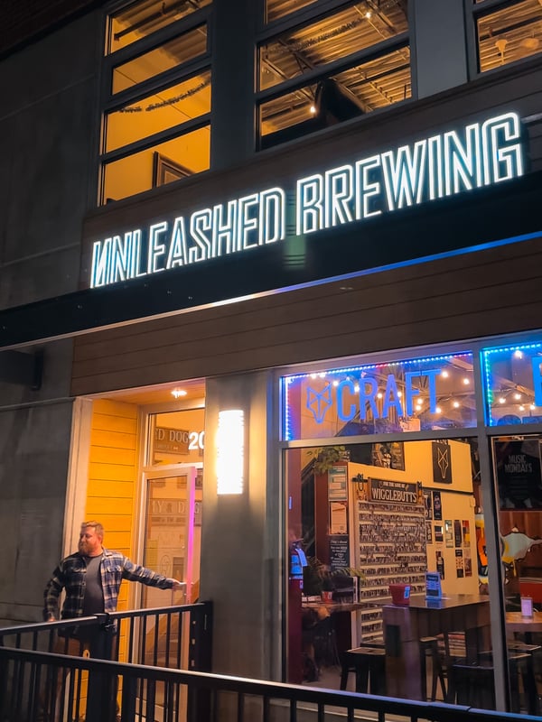 Man holds open a door for a brewery called Unleashed Brewing