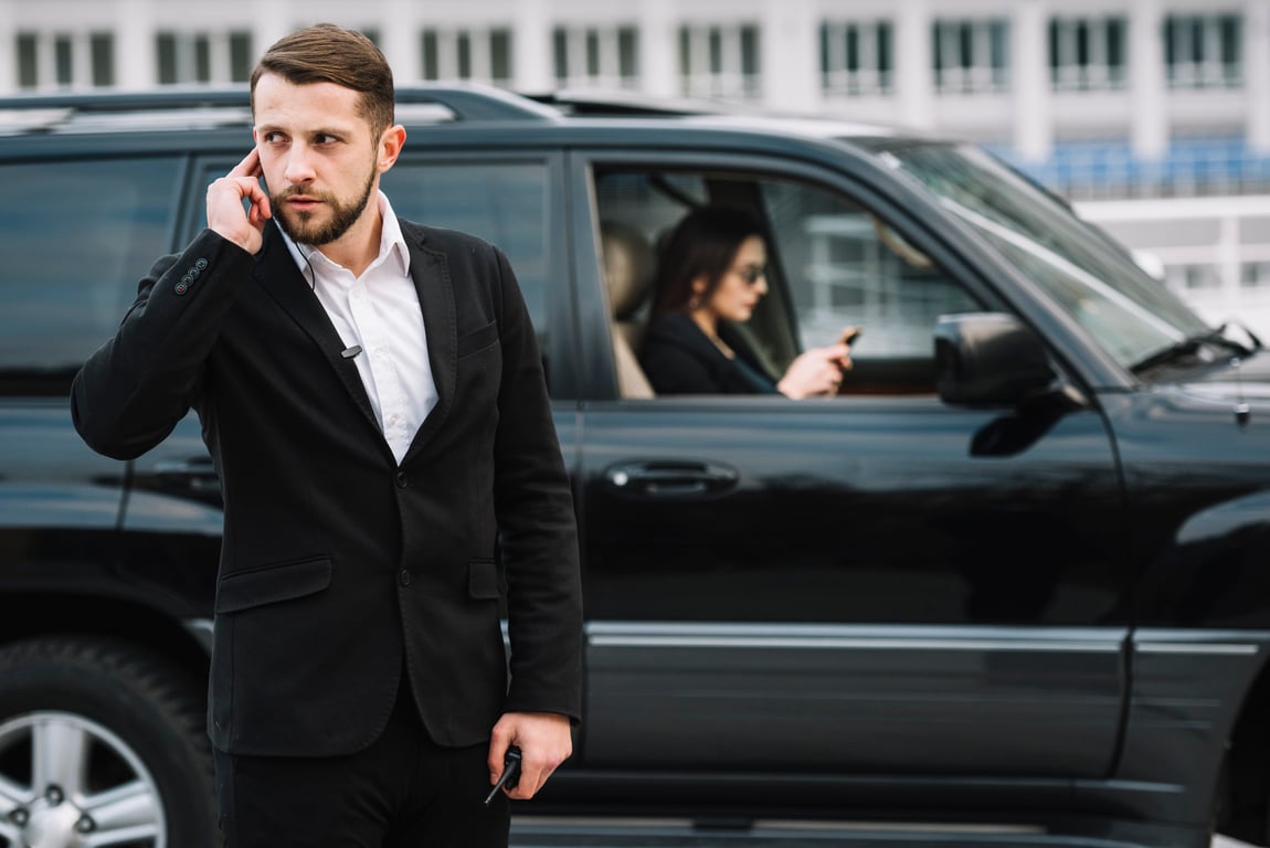 A security guard stands outside a vehicle as he listens to his earpiece