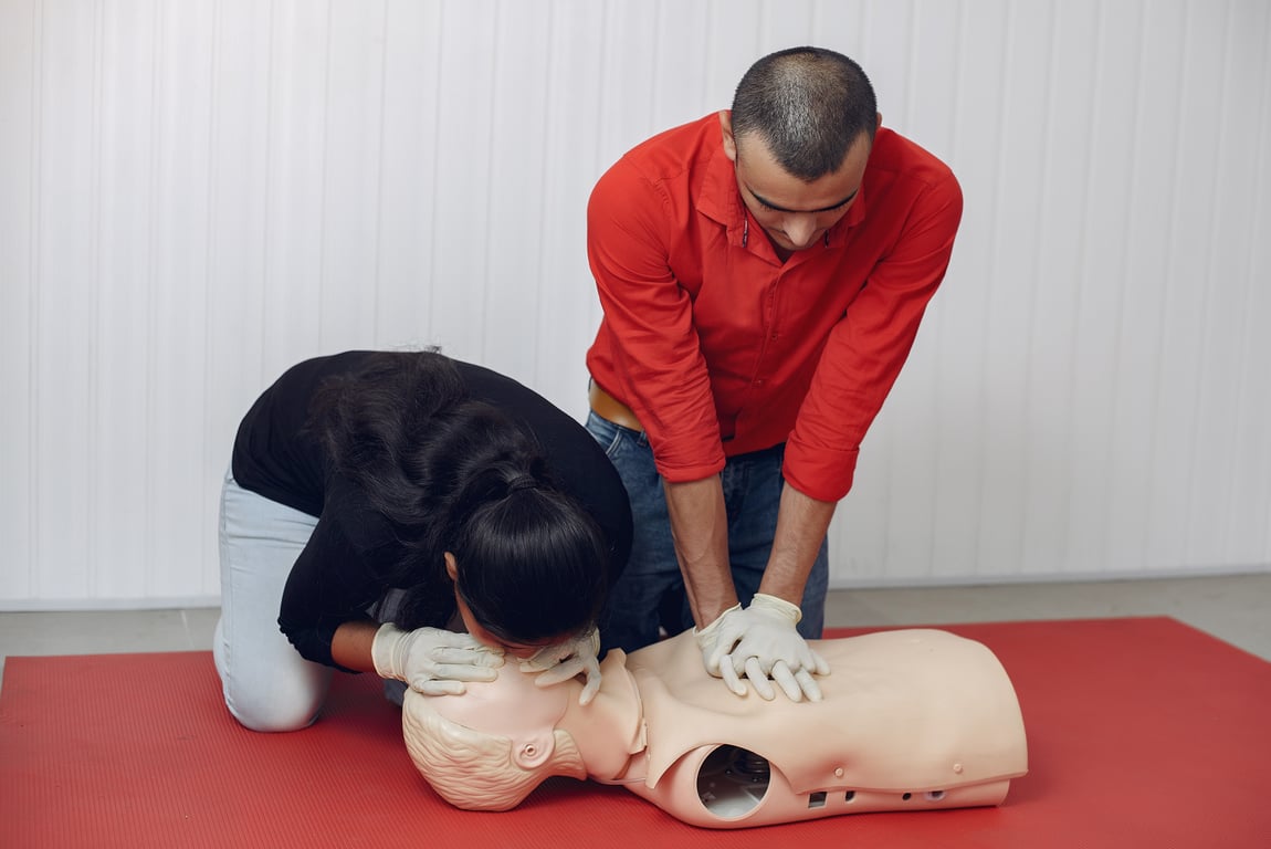 Two students simultaneously perform CPR on a training dummy.