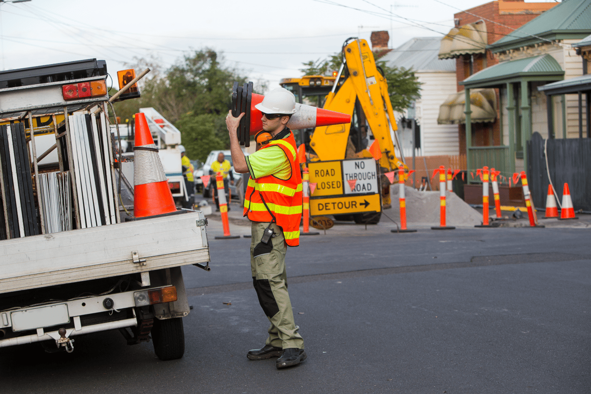 A traffic controller wearing a high visibility vest carrying traffic cones from a traffic vehicle