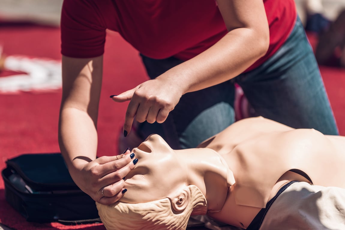 A person holding a CPR dummy by the nose, lifting its chin upwards