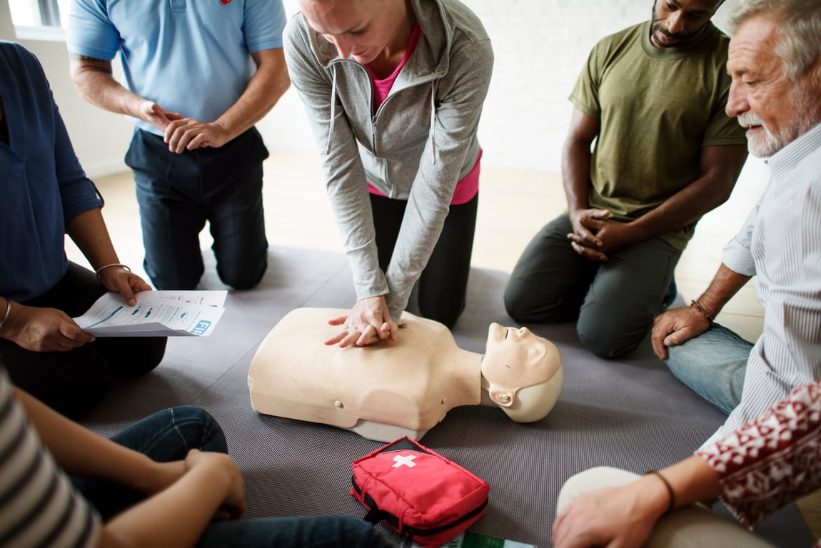 A group of students watch as one performs compressions on a CPR dummy