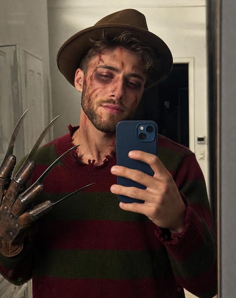 Generate a completely new, photorealistic iPhone mirror selfie of the person in the uploaded facial reference, dressed in a Freddy Krueger-inspired Halloween costume.
CRITICAL — NATURAL FACE, NOT FACE SWAP: Use the reference image only to understand the person’s identity. Generate a fresh, three-dimensional face naturally belonging to the photographed person. Do not copy, cut out, paste, overlay, or transplant the original face pixels. Preserve the person’s recognizable facial characteristics while naturally adapting their expression, head angle, perspective, and facial anatomy to the new selfie.
The face must be rendered as part of the original photograph, with naturally connected temples, ears, jawline, neck, and hairline. Match the lighting and focus across the entire head. Halloween makeup must follow the actual contours of the face, with realistic texture over the skin rather than appearing as a separate digital layer.
HALLOWEEN APPEARANCE: A tan vintage fedora, an oversized dark olive-green and burgundy striped knitted sweater, and dark pants. Add scary Freddy Krueger-inspired makeup with ashy pale skin, dark bruised eye sockets, irregular red scratch marks, realistic smudged bloody streaks, and subtle scar details. Keep it convincing as real Halloween makeup applied by hand.
POSE AND COMPOSITION: A casual, slightly tilted iPhone mirror selfie in a simple indoor hallway. Hold a blue dual-camera iPhone naturally in one hand, partially covering the lower face and chest. Raise the other hand beside the body, wearing a weathered brown leather horror glove with four long metallic blades. Frame from the hat to the upper thighs. Keep the same relaxed, casual mirror-selfie energy as a real personal photo.
LIGHTING: Ordinary overhead room lighting and natural phone-camera exposure. Realistic shadows beneath the hat brim, around the nose, under the chin, and along the neck. Natural reflections on the phone and glove. Consistent sharpness, grain, white balance, and color across the face, hair, clothing, and background.
REAL PHOTO QUALITY: Authentic iPhone mirror selfie, natural skin pores, slight asymmetry, imperfect hair strands, visible knit texture, subtle mirror dust, mild sensor grain, ordinary indoor colors, and unedited photographic realism. Avoid the glossy, overly smooth appearance of AI portraits.
DO NOT: Create a face-swap image, preserve the reference image’s original lighting, place a sharp face over a softer head, produce mismatched skin texture, blur the facial edges, create a floating face, beautify the identity, or make the result resemble a movie poster.
The final image should look as if the person genuinely dressed up for Halloween, stood in front of a mirror, and took one real photograph with their iPhone.