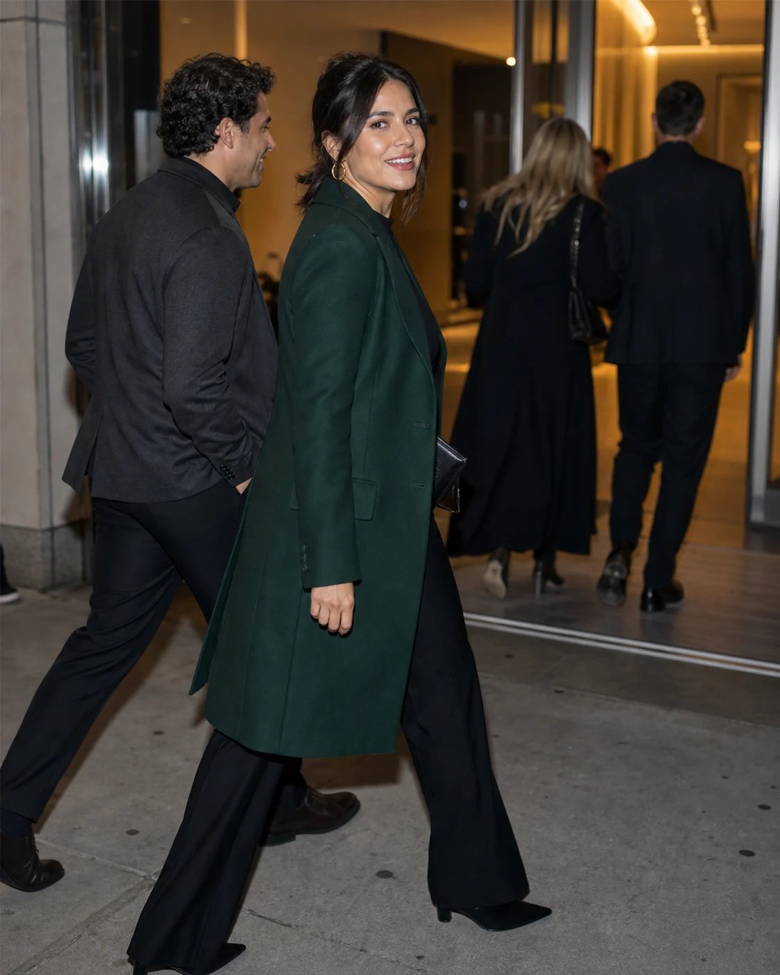 Two companions in coordinated dark coats walking toward a warmly lit theater entrance