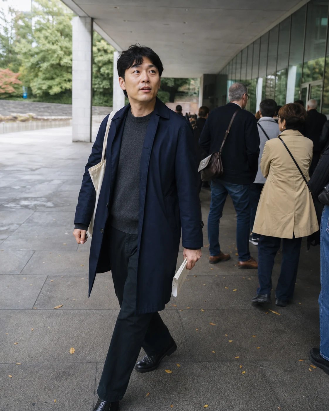 A filmgoer in a navy trench arriving for a daytime screening beneath a modern theater overhang