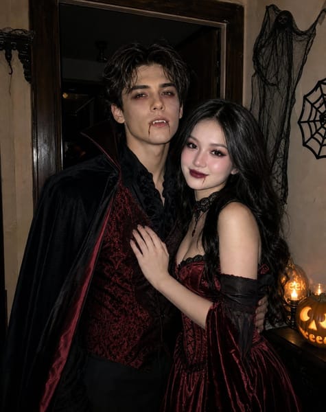 Create a single highly photorealistic Halloween vampire couple photograph using the two uploaded reference images for FACIAL IDENTITY ONLY.
IDENTITY — ABSOLUTE PRIORITY
Reference 1 is the man. Reference 2 is the woman.
Preserve both individuals’ exact recognizable facial anatomy, eye shapes, nose structures, lips, jawlines, natural skin tones and facial proportions. They must remain unmistakably the same two people.
Do not copy their original hairstyle, makeup, expression, pose, clothing, head angle, background or lighting. Completely restyle both individuals for the Halloween concept.
CONCEPT — REAL COUPLE IN VAMPIRE COSTUMES AT A HALLOWEEN PARTY
Create a believable candid photograph of a young couple dressed as sophisticated, slightly terrifying vampires at a real Halloween house party.
The man stands on the left, wearing a fitted black Victorian vampire cape with deep burgundy lining, a dark crimson brocade waistcoat, black shirt and tailored black trousers. His dark wavy hair is restyled with slightly messy, naturally separated strands falling around his forehead.
His vampire makeup is clearly visible: smoky charcoal eyeshadow around both eyes, subtle dark-red shading beneath the lower eyelids, a slightly pale theatrical complexion that still retains his natural skin texture, muted burgundy lips and a thin streak of realistic fake blood running from one corner of his mouth. Add small, believable vampire fangs visible through a slight parted-lip expression.
The woman stands on the right in a deep blood-red velvet gothic gown with a structured corset bodice, black lace detailing, elegant sleeves and a naturally flowing skirt. Her hair is styled into voluminous loose waves with a slightly messy side part, entirely different from her reference photograph.
Her Halloween makeup must be unmistakably vampiric: smoky black-and-burgundy eyeshadow, dark eyeliner, softly smudged lower lash line, deep wine-red lipstick, subtle contouring, slightly pale theatrical foundation with natural skin texture and a tiny streak of realistic fake blood near the corner of her lower lip. Her makeup should look professionally applied by a real Halloween makeup artist, not digitally painted.
COUPLE INTERACTION
The man has one arm naturally around her waist, pulling her slightly closer. She rests one hand against his chest, leaning comfortably into him. Their shoulders overlap, their bodies have natural contact and they share a subtle intimate expression.
The man looks directly toward the camera with a restrained vampire-like half-smile. The woman tilts her head slightly toward him, looking confidently into the camera.
Both faces must be clearly visible. Their expressions should feel spontaneous rather than staged.
LOCATION — AUTHENTIC HALLOWEEN PARTY
Replace the previous artificial hallway with a real, slightly imperfect older residential interior decorated for Halloween.
A dark wooden doorway, textured painted walls, a few casually arranged Halloween decorations, a small cluster of real pumpkins and subdued practical lighting. The space should feel like a genuine house where people have decorated for a party, not an elaborate gothic film set.
Avoid symmetrical architecture, perfect polished surfaces, excessive candles, artificial fog, fantasy castles, chandeliers, digital-looking decorations or unnecessary background people.
PHOTOGRAPHY — EXTREMELY IMPORTANT
Photograph this as if a friend took the picture using a modern smartphone with direct flash at an actual nighttime Halloween party.
Natural flash falloff, believable shadows behind the couple, slight ambient darkness, realistic skin texture, natural hair flyaways, detailed fabric textures and authentic photographic depth.
The flash should illuminate both faces clearly while leaving the background naturally darker.
Avoid excessive brightness, yellow lighting, orange cast, dramatic cinematic spotlights, studio lighting, glowing skin or overprocessed HDR.
Allow subtle photographic imperfections: slight natural grain, realistic fabric creases, uneven hair strands and small variations in skin texture.
The final photograph must resemble an authentic real-world Halloween party photograph, not an AI-generated fashion editorial.
COMPOSITION
Vertical 2:3 photograph, framed approximately from the knees upward. Both individuals are clearly visible, standing close together. Natural eye-level camera angle, realistic perspective and no exaggerated lens distortion.
STRICTLY AVOID
AI-generated appearance, CGI, digital painting, fantasy illustration, overly perfect faces, plastic skin, beauty filters, face swapping artifacts, floating hair, unrealistic costumes, fake-looking blood, distorted hands, exaggerated red eyes, artificial backgrounds, extreme cinematic grading, yellow lighting, washed-out skin, identical expressions, stiff posing, pasted faces or identity changes.
FINAL PRIORITY
The photograph must convincingly look like the exact two reference individuals attending a real Halloween party together, wearing coordinated vampire costumes with clearly visible professional Halloween makeup. Preserve facial identity while completely transforming their styling, expressions and surroundings.