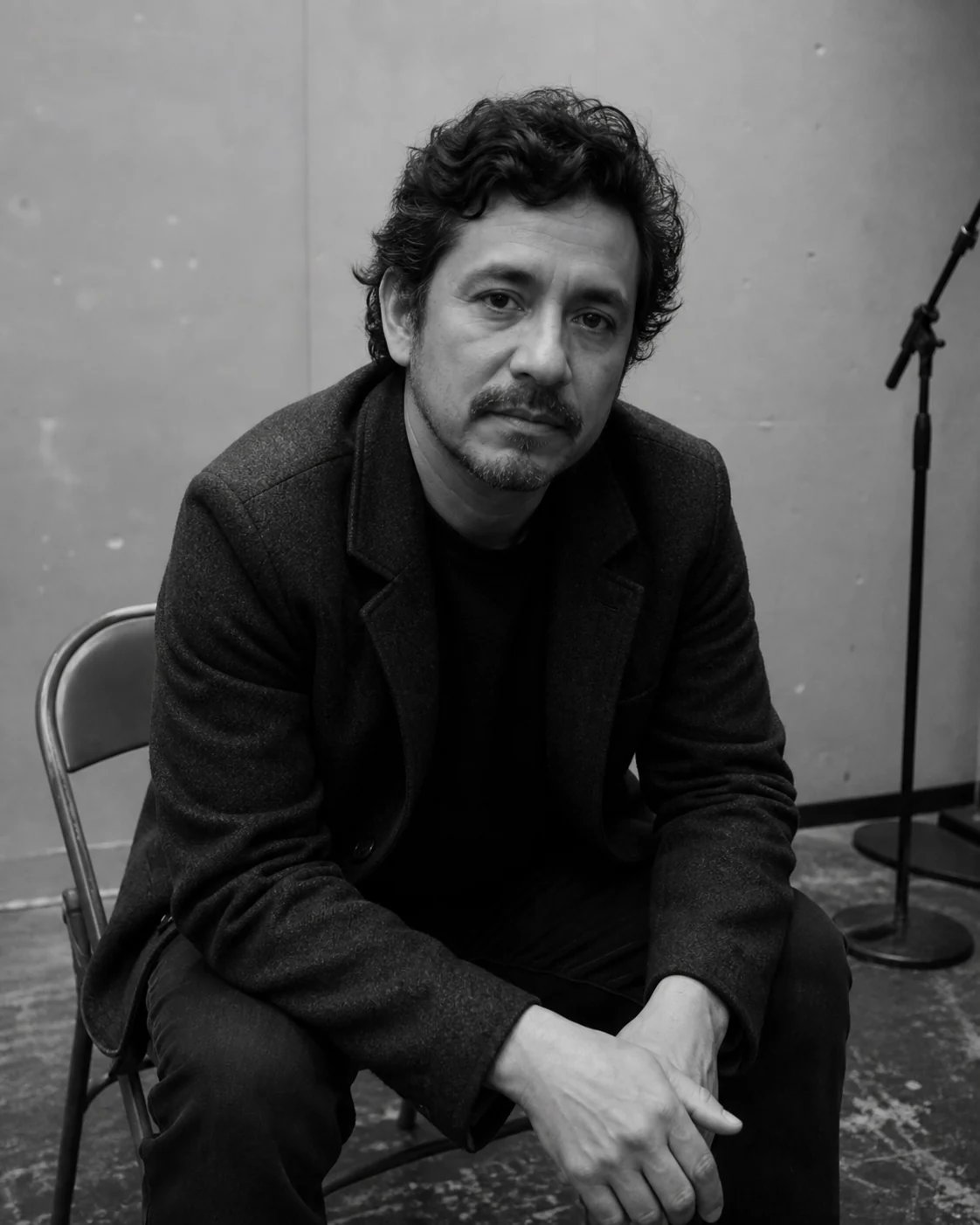 A thoughtful filmmaker seated on a folding chair in a plain black-and-white backstage portrait