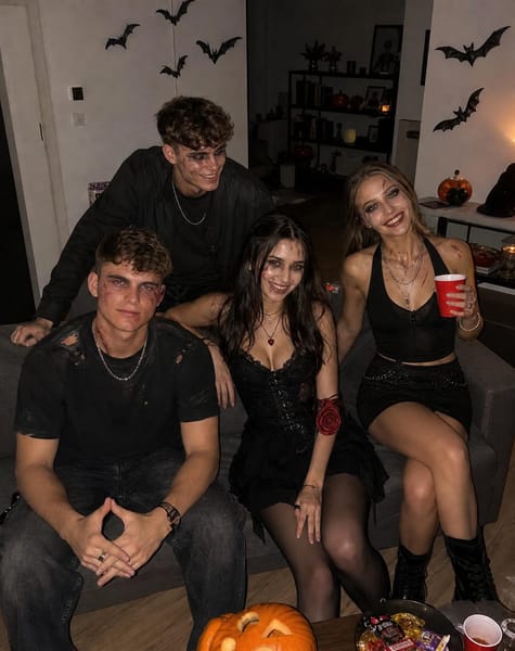 Transform the provided reference group photo into a completely new, ultra-realistic candid iPhone photograph of the SAME four friends — exactly two girls and two boys — attending a casual Halloween house party.
IDENTITY REFERENCE ONLY: Use the uploaded group photo exclusively to preserve the identities of all four people, including their recognizable facial features, natural skin tones, and hairstyles. Do NOT copy the original clothing, outfits, accessories, poses, body positions, background, location, lighting, or composition. Create an entirely new photograph from scratch while keeping all four people recognizable. Do not paste faces onto generated bodies. Reconstruct each face naturally, with realistic skin texture, matching shadows, and consistent camera perspective.
NEW HALLOWEEN OUTFITS: Give all four friends completely different clothes from the reference photograph. The girls wear stylish Halloween outfits such as a black gothic mini dress with sheer tights and a dark red accessory, and a fitted black top with a black skirt, layered silver jewelry, and dark boots. The boys wear a black distressed T-shirt with dark jeans and a dark oversized jacket with black trousers. Make the outfits fashionable, believable, and individually styled. Do not reproduce any garment or accessory from the original reference photo.
SCARY MAKEUP: All four have striking, genuinely scary Halloween makeup: pale ashy skin, deep black smoky eyes, smudged dark makeup, realistic fake-blood streaks, fine scratches, and individual horror details. Each person’s makeup should be different. Preserve their recognizable faces and realistic skin texture. No beauty-filter skin, no pasted-on makeup, and no exaggerated fantasy effects.
SCENE: A normal friend’s house during a Halloween party at night. A slightly messy living room with a real-looking sofa, a coffee table with Halloween sweets and plastic decorations, a few carved pumpkins, paper bats taped to the wall, scattered party cups, and ordinary household furniture. It should feel like a real home where friends are celebrating, NOT an abandoned mansion, haunted castle, professional photoshoot set, or artificial studio.
NATURAL GROUP POSE: One girl sits casually on the arm of the sofa, the other stands beside her holding a drink cup. One boy sits forward on the sofa while the other leans casually against its back. Everyone has a different expression: one laughs slightly, one gives a creepy smile, another looks directly into the camera, and the fourth looks toward a friend. Their body language should feel spontaneous and comfortable, like someone suddenly took a picture during the party. All four people must be visible, with natural proportions and realistic physical interaction.
CAMERA AND LIGHTING: An authentic handheld iPhone photo taken with direct phone flash. Faces and nearby clothing are illuminated naturally by the flash, while the room behind them remains dim and realistic. Natural falloff into darkness, believable shadows, subtle smartphone grain, slight imperfections, realistic reflections, and ordinary indoor color. No cinematic color grading, no artificial red lighting, no fog, no smoke, no haze, no glowing effects, and no dramatic movie-style spotlights.
FINAL RESULT: A genuinely believable, slightly imperfect Halloween party snapshot of four real friends. New outfits, new poses, a completely new setting, recognizable identities, and scary makeup. It must look like a photo someone casually took on an iPhone at a real house party — NOT an AI-generated poster, NOT a copy of the reference photograph, and NOT the original outfits transferred into a new background.