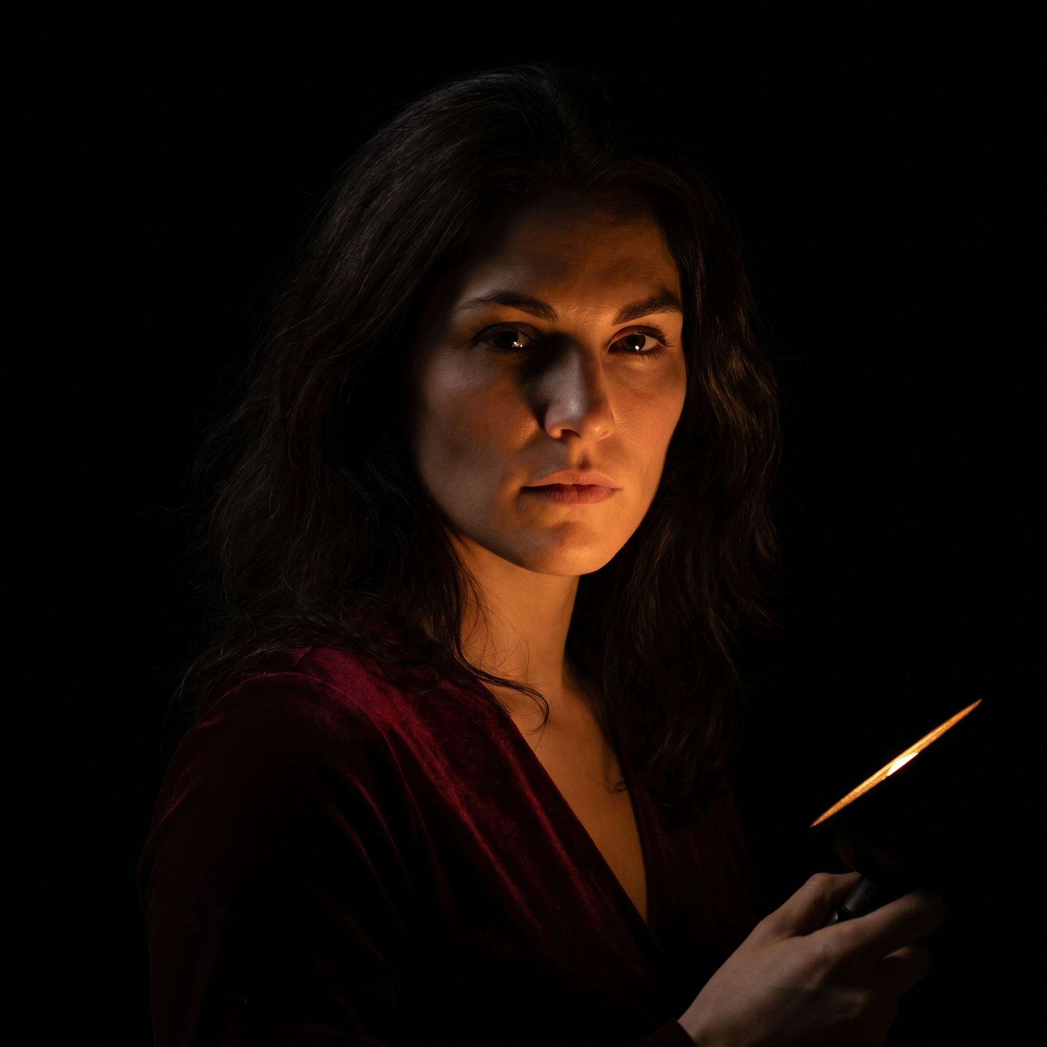 Female portrait, chiaroscuro, single motivated candle light from below right, warm amber illumination catching underside of jaw and cheekbones, subject emerging from absolute darkness