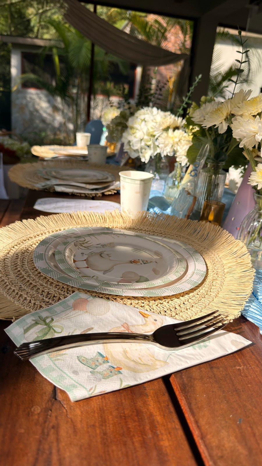 Lugar de mesa azul con vajilla de gansos, fibras naturales y flores claras preparado por ETERIA.