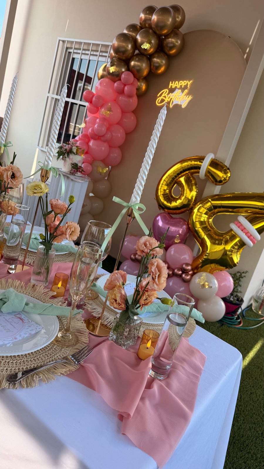 Escenario rosa de cumpleaños con mesa floral, velas altas y globos dorados diseñado por ETERIA.