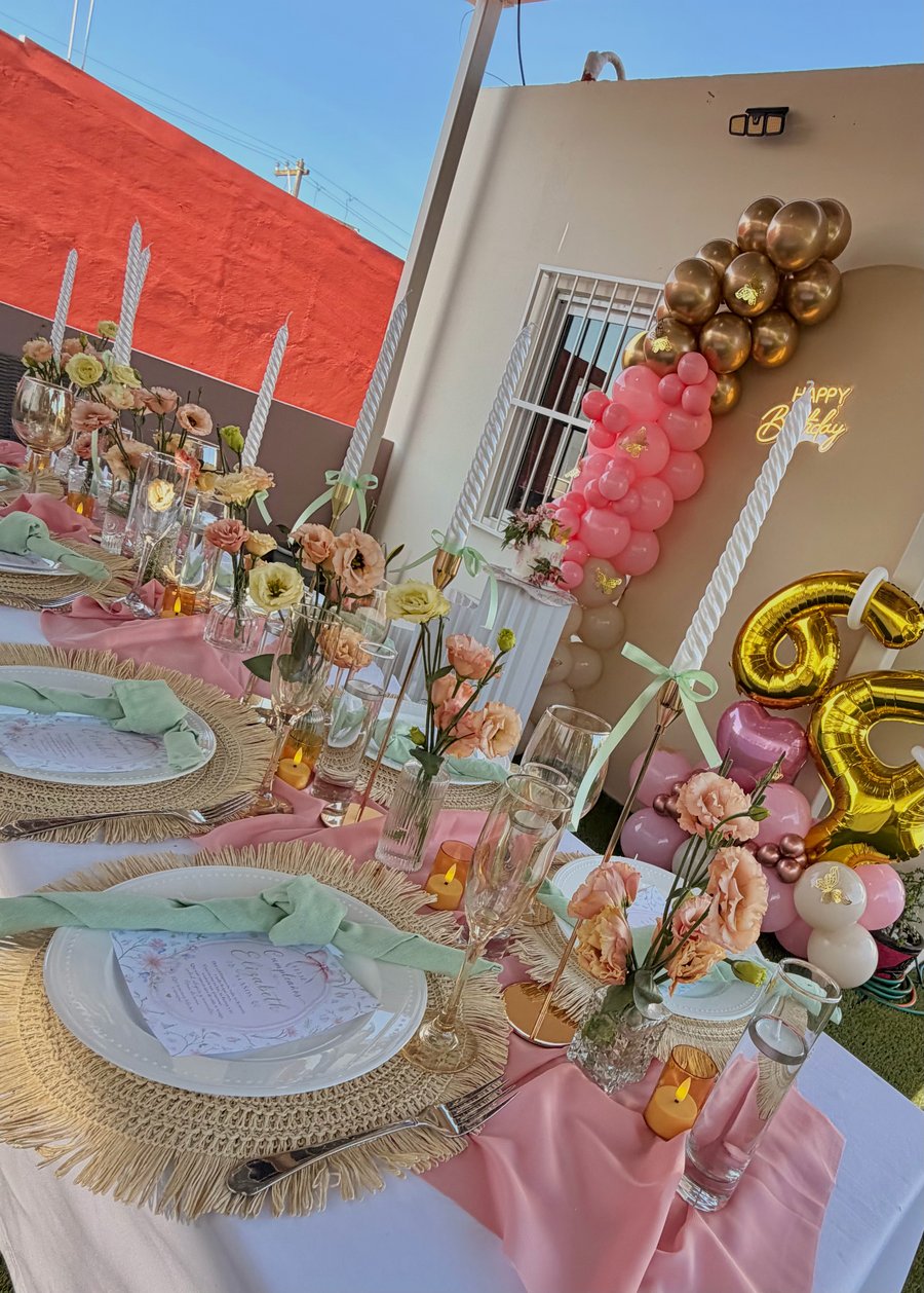 Mesa pastel y backdrop de cumpleaños con globos rosa y dorado en una escena completa de ETERIA.