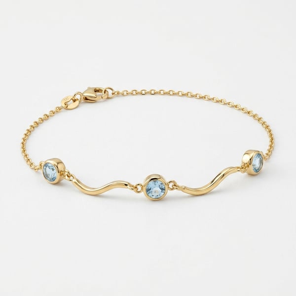 18K gold fluid wave anklet with three bezel-set round aquamarine gemstones on a white background.