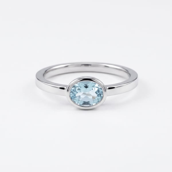 Studio shot of Saqiba sterling silver engagement ring with horizontal east-west oval aquamarine stone in bezel setting on white background.
