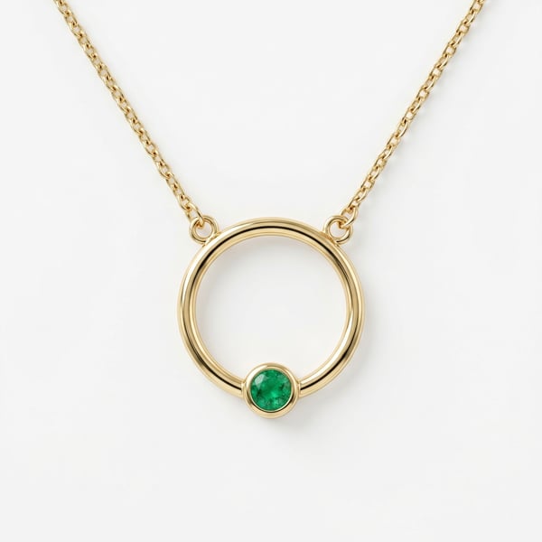 Studio shot of Loulou 18K gold necklace with a mini sleek hoop pendant and a bezel-set green emerald on a fine chain on white background.