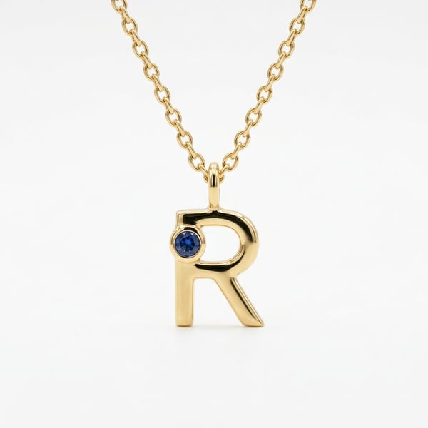 18K gold letter R initial necklace with a 3 mm blue sapphire on a plain white background.