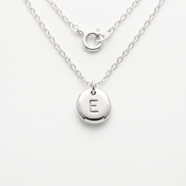 Studio close-up of a sterling silver kids initial E pebble necklace on a plain white background.