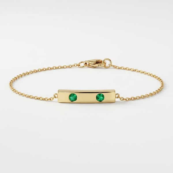 Studio shot of the Sausan 18K gold geometric bar anklet with two small natural emeralds on a white background.