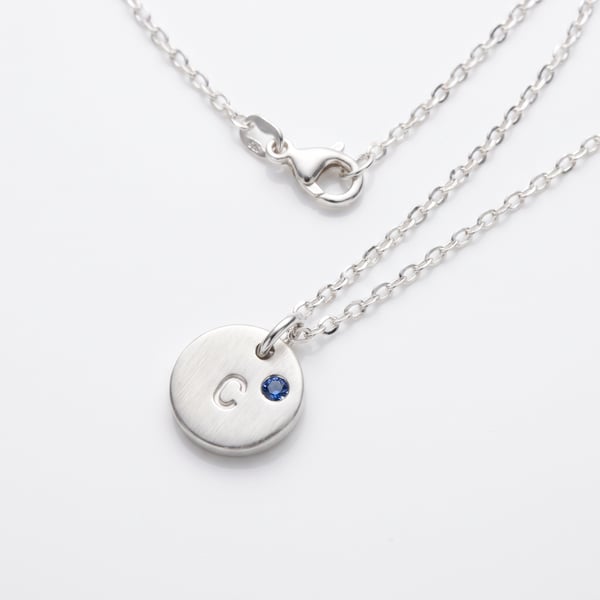 Sterling silver 8mm round disc pendant stamped with letter C and flush-set sapphire on a fine chain.