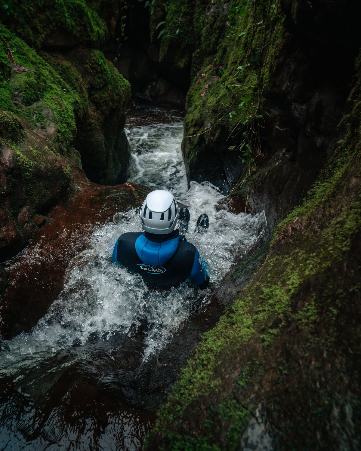 Canyoning guest slides into beutiful canyon pool surrounded by moss covered rocks in Dollar Glen