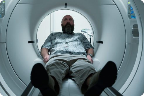 A man with a beard lies inside an MRI scanner machine. He appears relaxed and is wearing casual clothes.