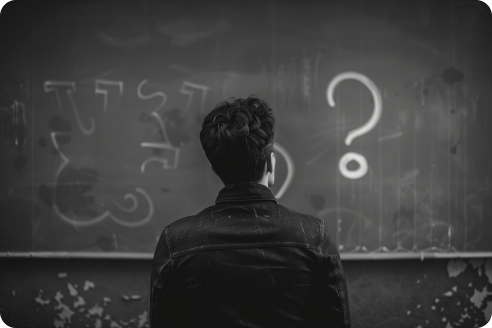 A man standing in front of a chalk board with a "?" written on it, black and white.