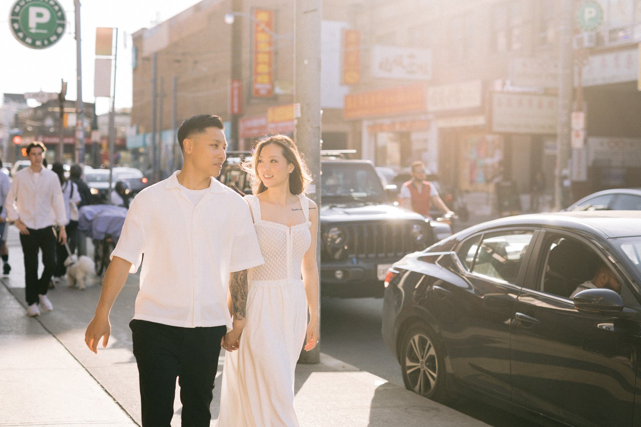 Engagement session — couple walking hand in hand down a Toronto street at golden hour, soft sunlight behind them