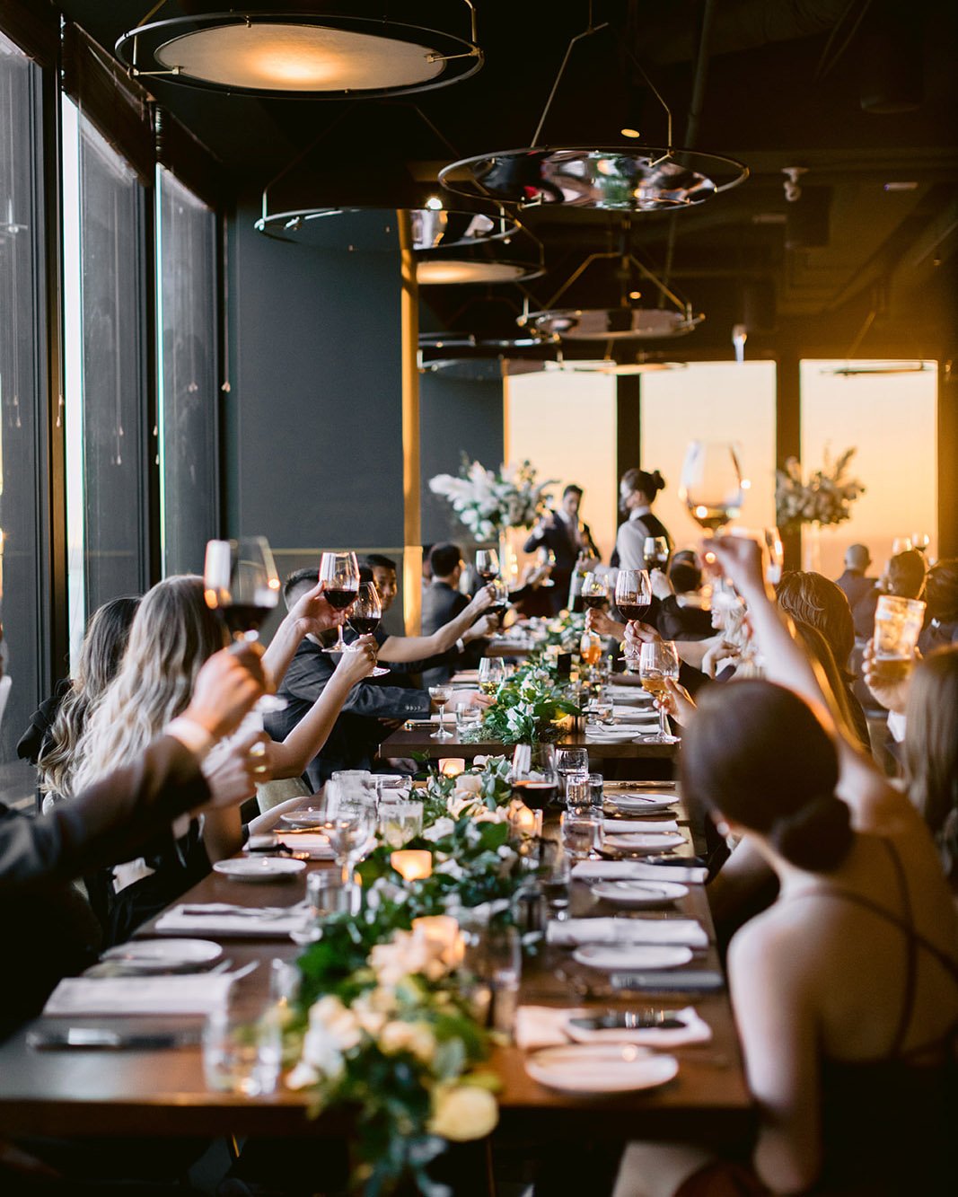 Guests raising glasses at Canoe restaurant, sunlight catching the glassware