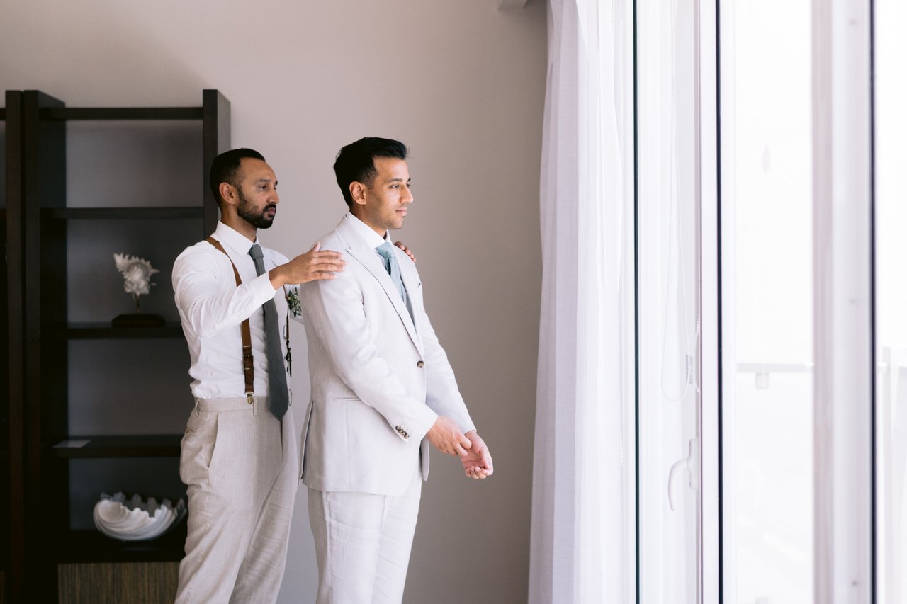 A groomsman straightening Hussain&rsquo;s tie by the window