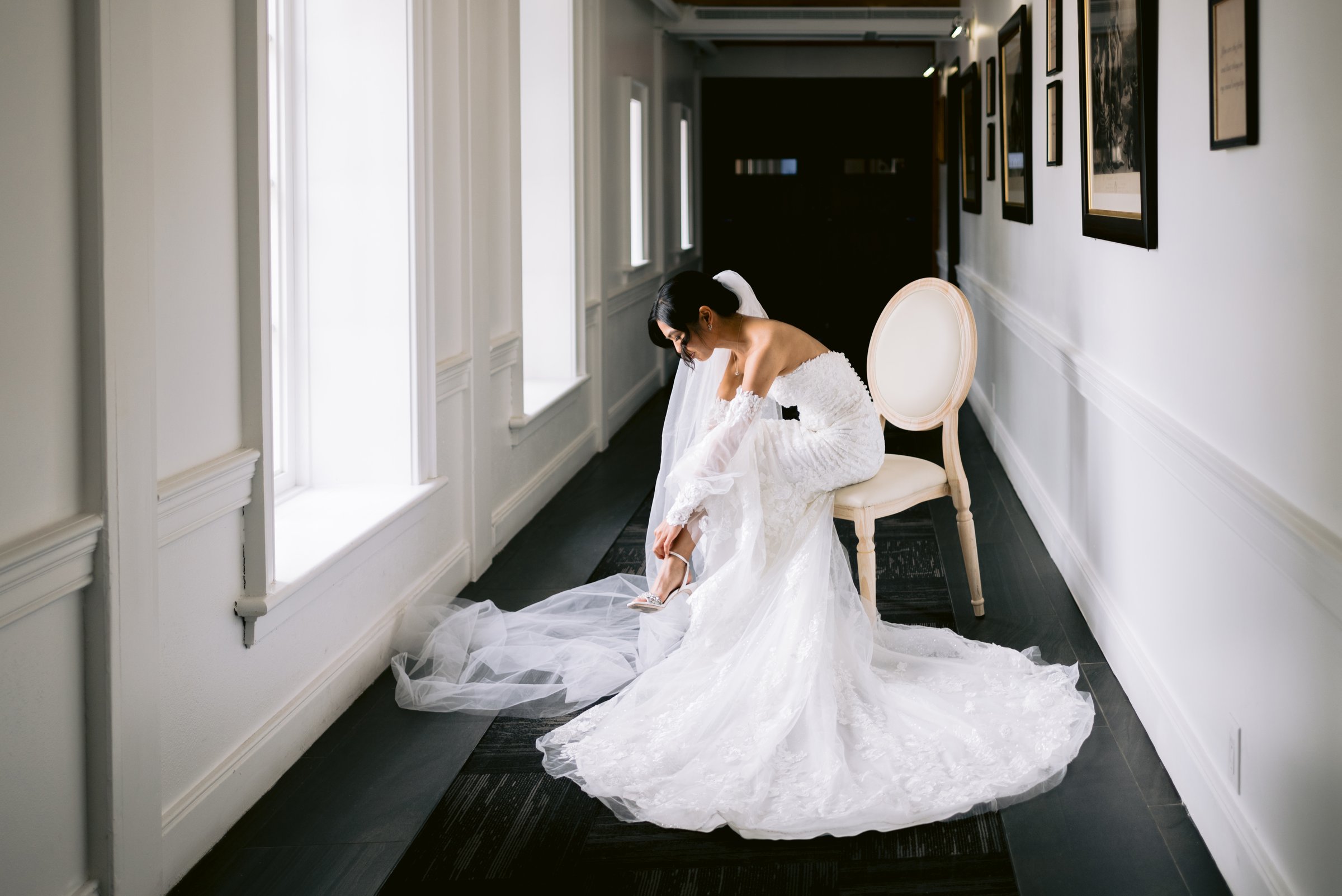 Kat seated on a chair in the gallery hallway, her gown and veil spread across the floor at The Doctor&rsquo;s House